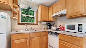 Una cocina con armarios de madera, estufa, microondas y ventana con vista a zonas verdes.