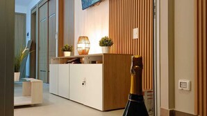 Una sala de estar moderna con un televisor montado en la pared, un mueble de madera y una botella de vino Valodin sobre una mesa tejida.