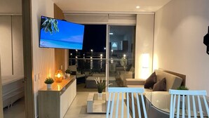 Una sala moderna con televisor de pantalla plana, sofá, mesa de centro y balcón con vista al cielo nocturno.