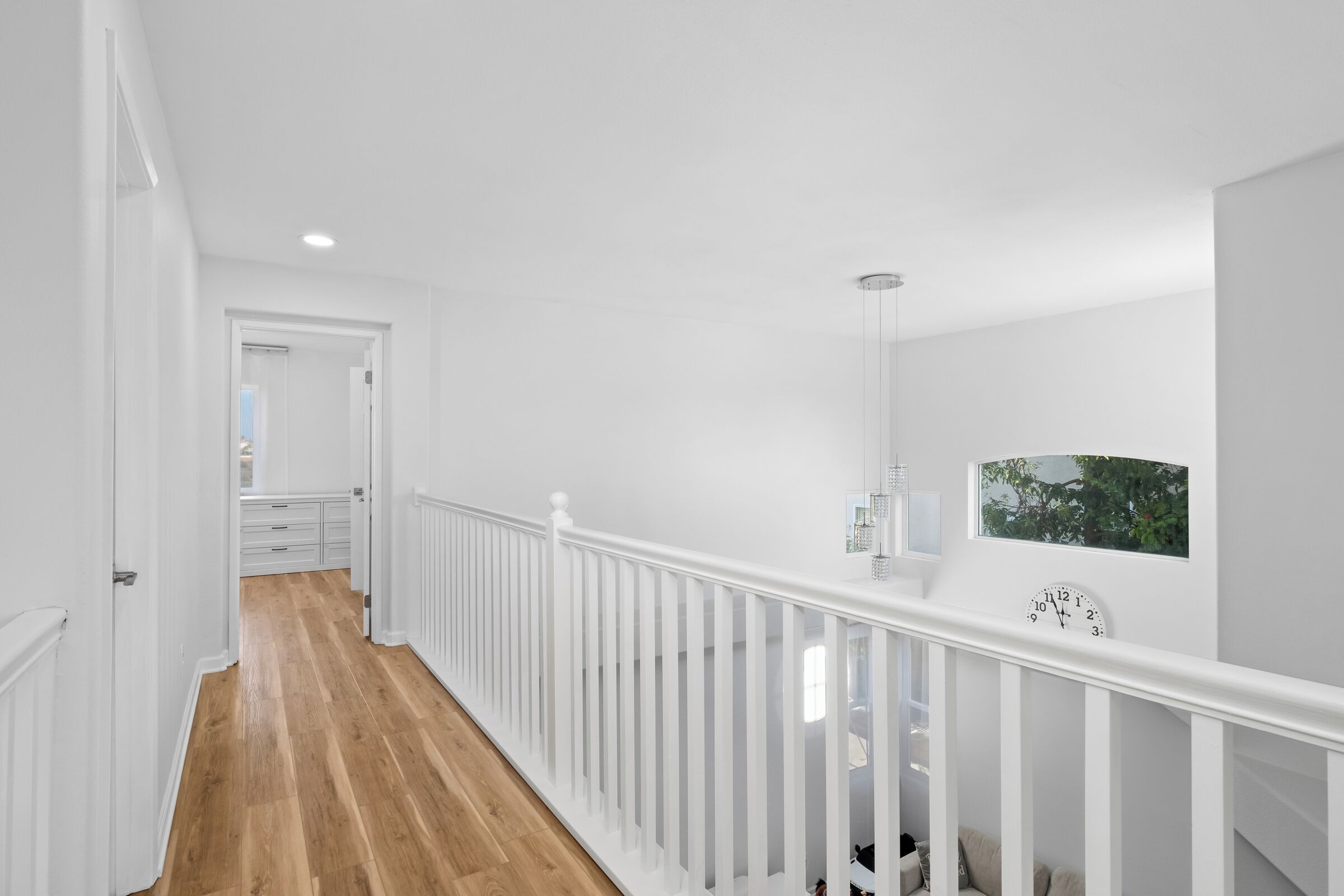 A white interior hallway with wooden flooring, white railings, and a clock on the wall.