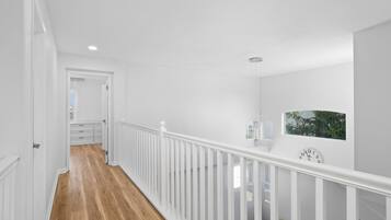 A white interior hallway with wooden flooring, white railings, and a clock on the wall.