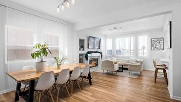 A spacious living room with a fireplace, a dining area with a wooden table and chairs, and a modern white color scheme.