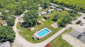 An aerial view of a campground with RVs, a swimming pool, and a dirt road.