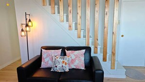 A black leather sofa with floral-patterned cushions, a wooden staircase with white railings, and a floor lamp with multiple bulbs.