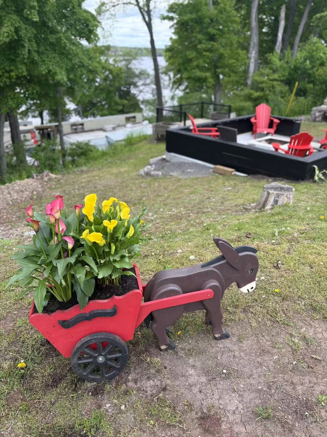 A garden with a red cart filled with yellow flowers and a donkey figurine.