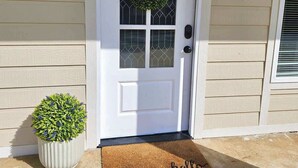 A white door with a wreath, a potted plant, and a 'hello' mat.