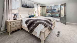 Une chambre avec un grand lit, une table de chevet, une lampe et une vue sur l’extérieur.