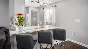 Une cuisine moderne avec un plan de travail en marbre, deux tabourets de bar, un vase de tulipes et une suspension lumineuse.