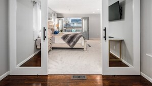 Une chambre à coucher comprenant un lit, une commode, un téléviseur et une porte coulissante donnant sur un balcon.