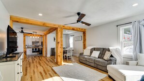 Ein geräumiger Wohnbereich mit Holzboden, einem grauen Sofa, einem weißen Sessel und einem Esstisch.