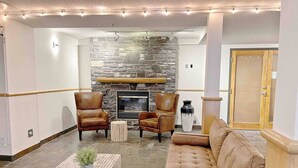 Un salon chaleureux avec une cheminée en pierre, des fauteuils en cuir, un canapé capitonné et une table basse carrelée.