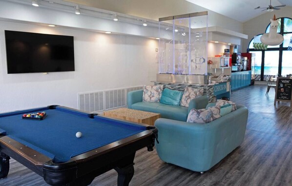 A pool table with balls, a sofa with cushions, a television mounted on the wall, and a reception desk with a sign. - 3BR Resort Oasis: Pools, Gym & Sunset Views (St. George)
