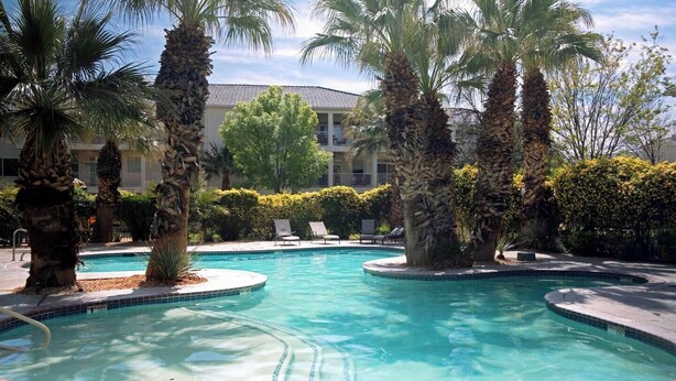 A pool area with palm trees, lounge chairs, and a building in the background. - 3BR Resort Oasis: Pools, Gym & Sunset Views (St. George)
