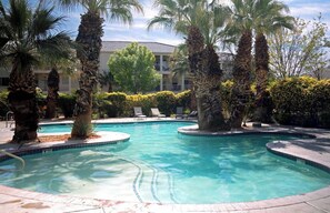 A pool area with palm trees, lounge chairs, and a building in the background. - 3BR Resort Oasis: Pools, Gym & Sunset Views (St. George)