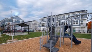 A playground with a slide and climbing structures, surrounded by a covered seating area and a parking lot with cars. - Modern 3BR Retreat | Mtn Views & Garage Parking (South Salt Lake)