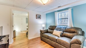 A living room with a brown leather couch, a wooden floor, a lamp, and a window with curtains. - 2 Mi to Toccoa Falls: Cozy Getaway w/ Yard! (Toccoa)
