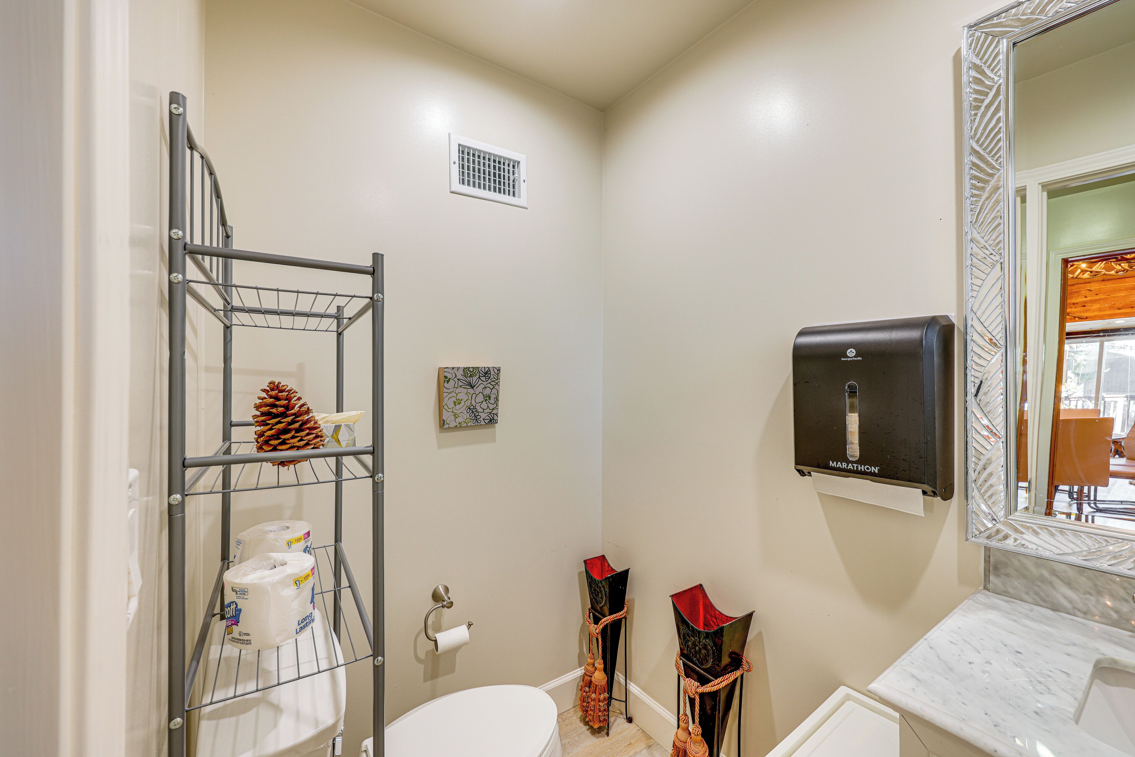Un bagno con il water, uno scaffale con carta igienica, un asciugamani ad aria e uno specchio con cornice decorativa.