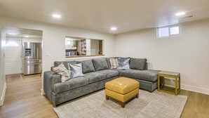 A modern living room with a sectional sofa, a small ottoman, and a kitchen area in the background. - Scenic Patio & Views! Stay 10 Mi to Nordic Valley (Ogden)