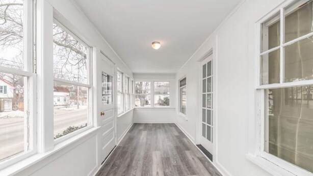 Un couloir aux murs blancs et au plancher en bois, avec de grandes fenêtres de chaque côté et un luminaire au plafond.
