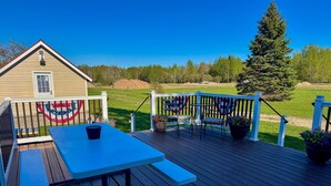 A deck with a picnic table and chairs, a flag, and a view of a green field and trees.