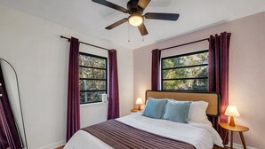 A bedroom with a bed, two bedside lamps, a ceiling fan, and windows with curtains. - Spacious 4BD - Central Stay w/ Backyard & Games (Tallahassee)