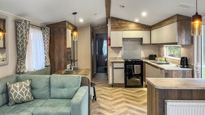 A compact kitchenette with a stove, oven, and sink. There is a sofa with patterned cushions and a small table with a basket.