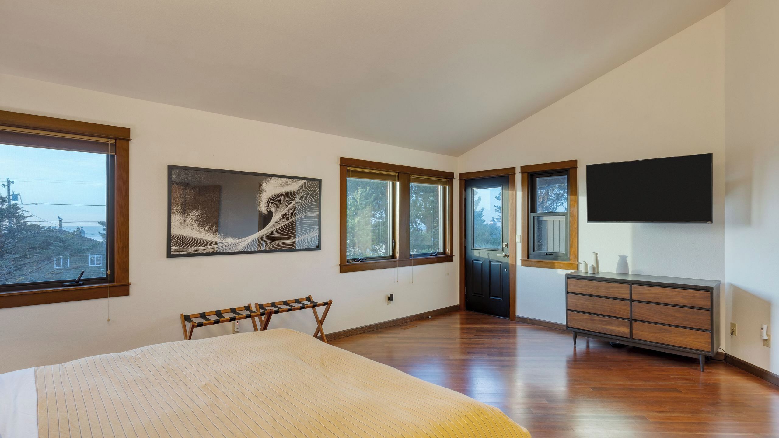 A bedroom with a bed, a dresser, a TV, and large windows.