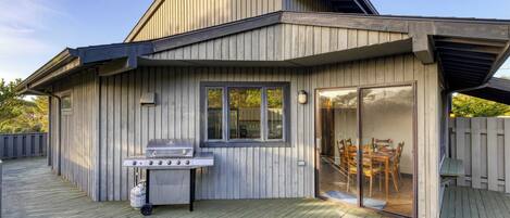A modern house with a wooden exterior, a covered patio, and a barbecue grill.