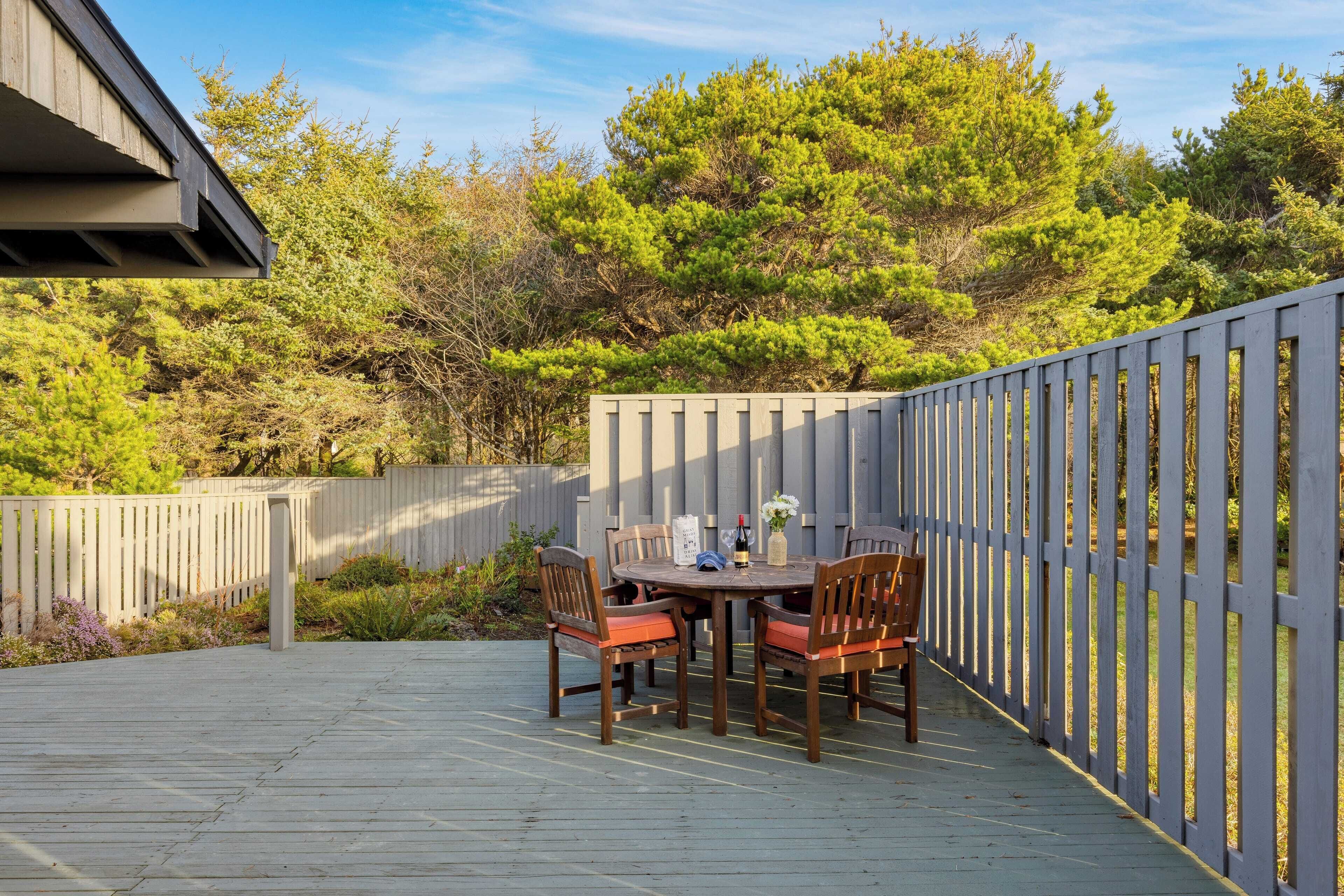 Una terraza al aire libre con una mesa y sillas de madera, rodeada por un cerco de madera y árboles.