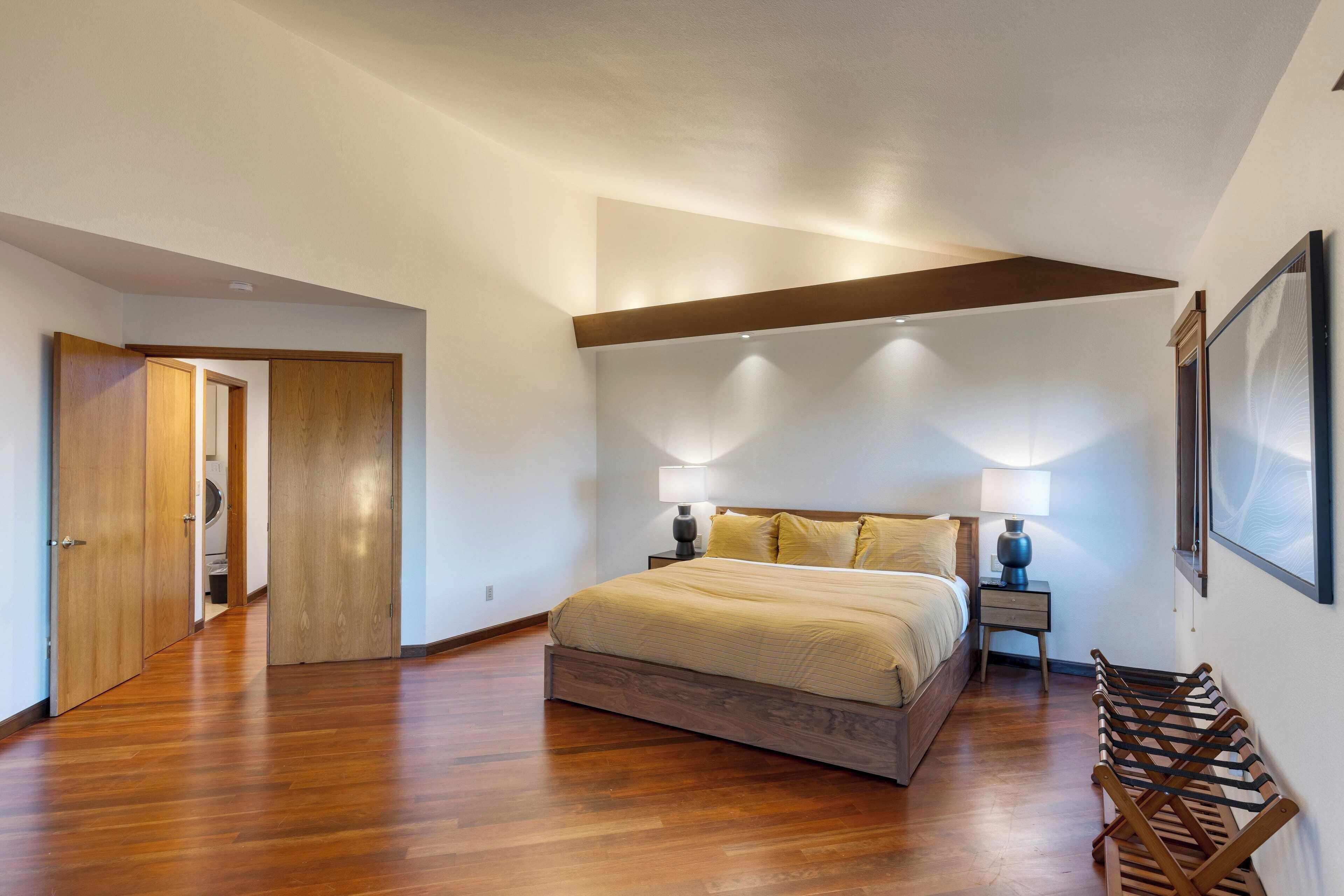 A bedroom with a wooden floor, a bed with a wooden frame, two bedside tables with lamps, and a wooden bench.