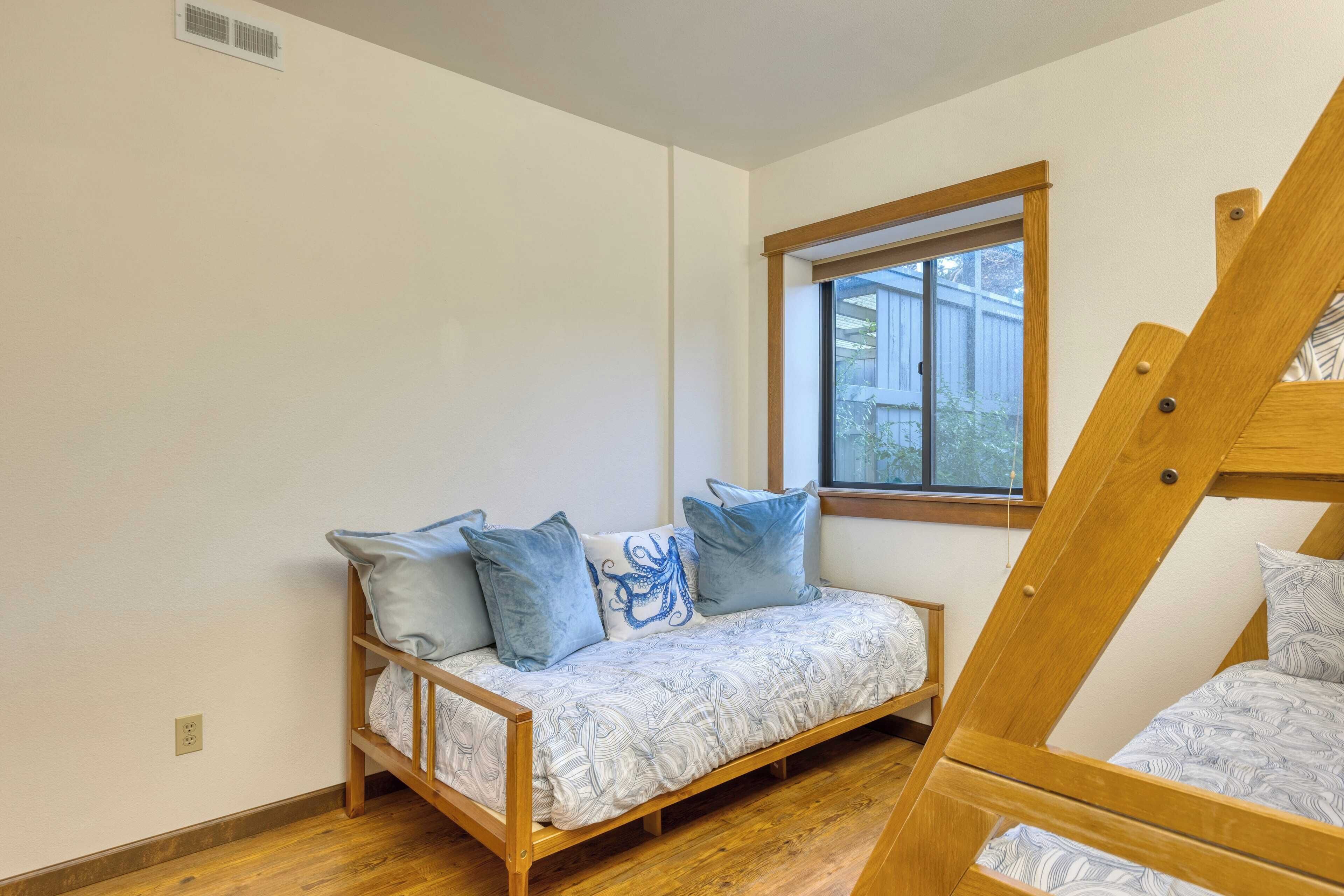 A room with a wooden bunk bed, a sofa bed with patterned bedding, and a window providing natural light.