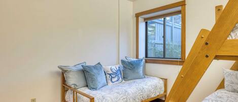 A room with a wooden bunk bed, a sofa bed with patterned bedding, and a window providing natural light.