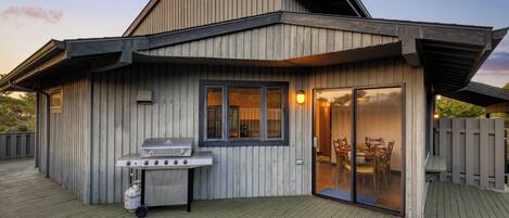 A modern house with a wooden exterior, a deck, and a sliding glass door leading to an indoor dining area.