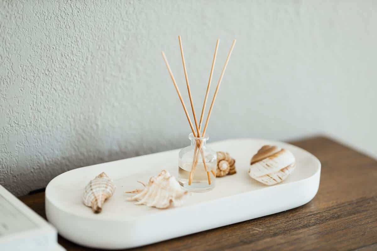 Un plateau rectangulaire blanc sur lequel se trouvent une bouteille en verre de diffuseur à bâtonnets et plusieurs coquillages, le tout posé sur une surface en bois.