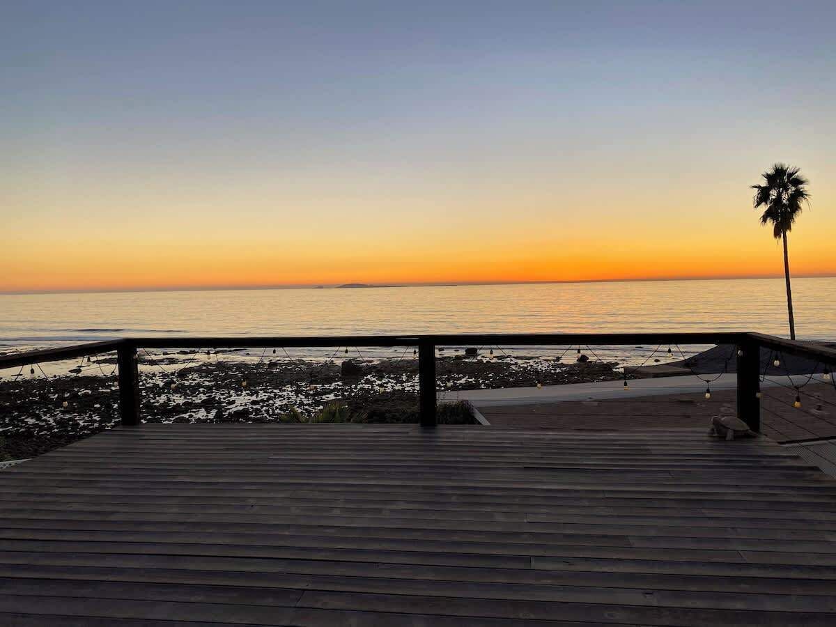 Une promenade en bois menant à une plage, avec un palmier et des guirlandes lumineuses.