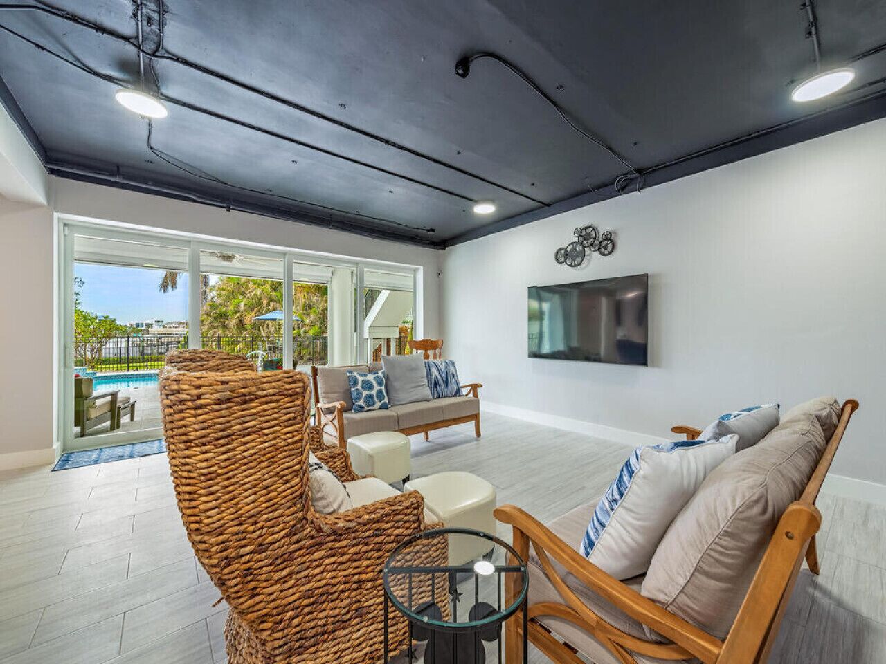 Ein modernes Wohnzimmer mit Korbmöbeln, einem Flachbildfernseher und Blick auf einen Pool.