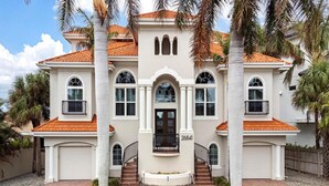 A two-story house with a red-tiled roof, white exterior walls, and a central entrance with a black door. - Luxury Waterfront Retreat - 6BR, Heated Pool, Walk to Beach (Bonita Springs)