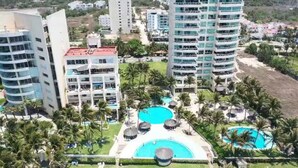 Un resort con varios edificios altos, una piscina central y palmeras que lo rodean.
