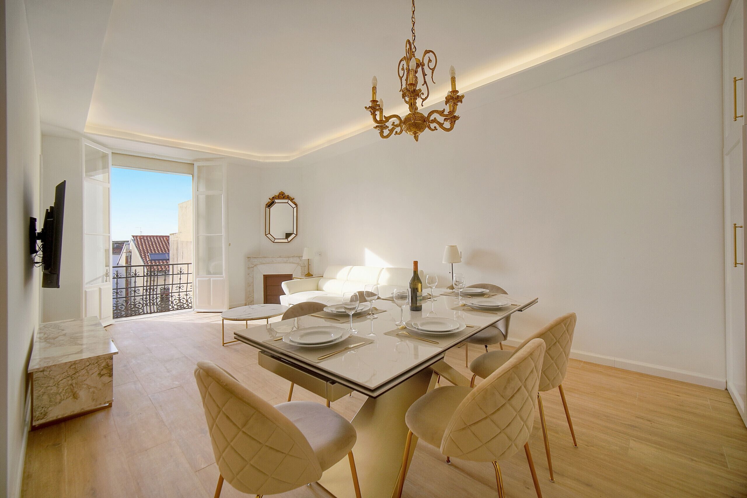 A modern dining room with a glass table, white chairs, and a chandelier.