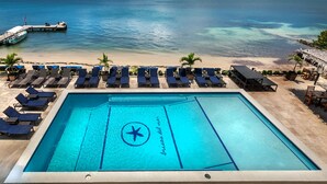 Une piscine ornée d’un logo en forme d’étoile et du texte « brise del mar » sur le fond, entourée de chaises longues et offrant une vue sur l’océan.