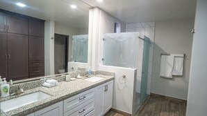 Une salle de bain moderne avec un comptoir en granit, des armoires blanches, un grand miroir et une cabine de douche en verre.