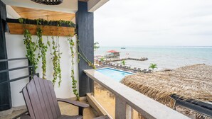 Un balcon avec vue sur la mer, une piscine et un espace doté d’un toit de chaume.