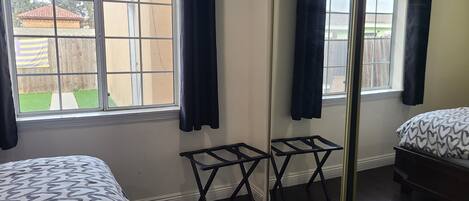A bedroom with a bed, a small table, a mirror, and a window with curtains.