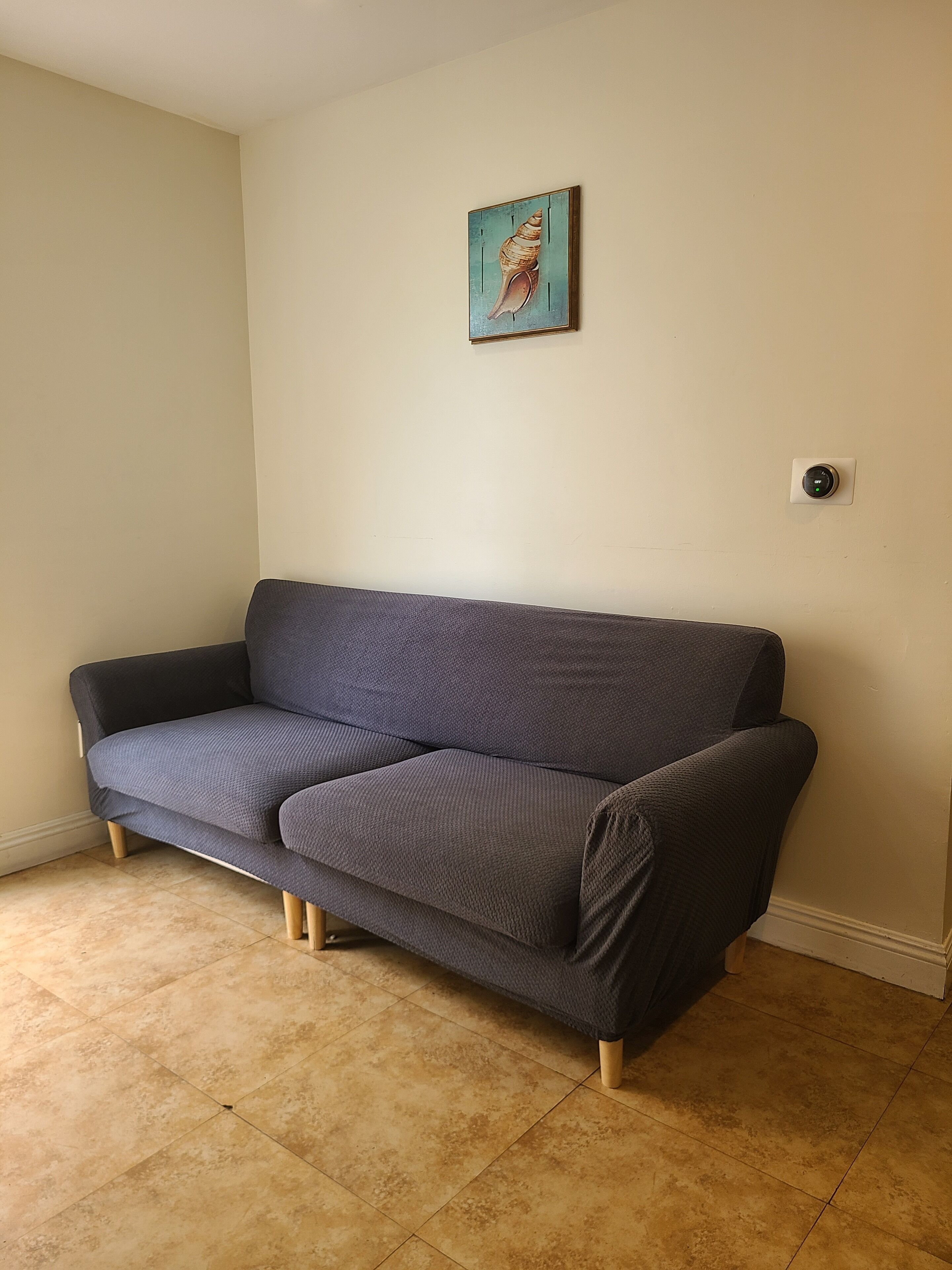 Un sofá gris en una habitación con paredes beige y suelo de baldosas.