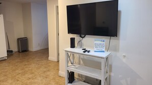 A room with a mounted flat-screen TV, a white console table with a sign, a trash can, and a broom. - Cozy Cottage, 2-bedroom duplex in delightful Beach City with WiFi, AC (Torrance)