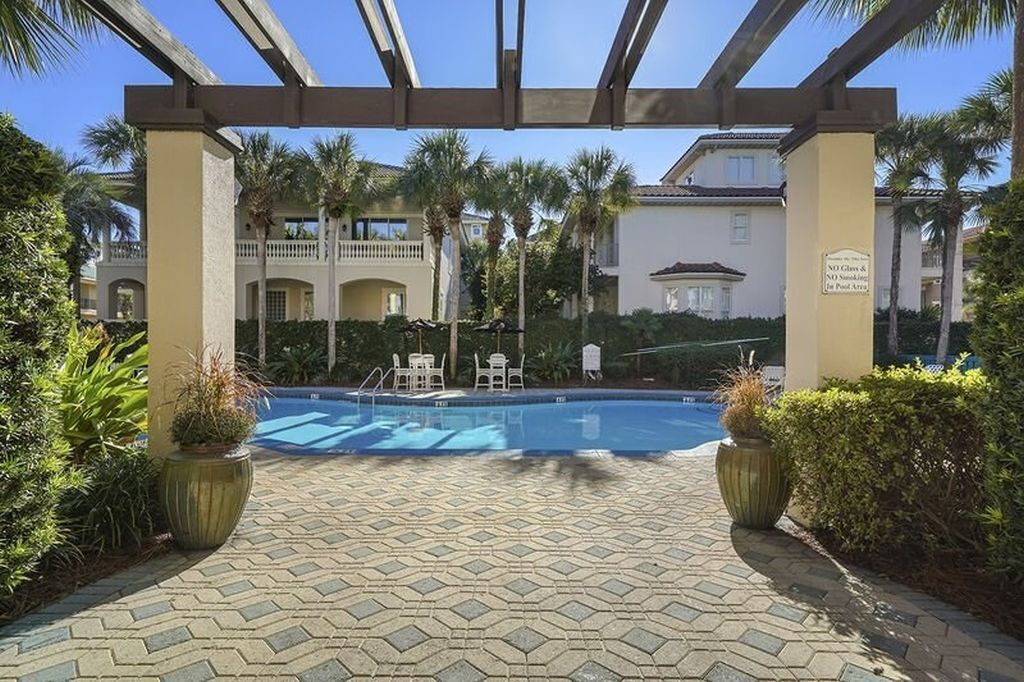 Zona de piscina amb sòl de rajola, palmeres i una estructura de pergola.