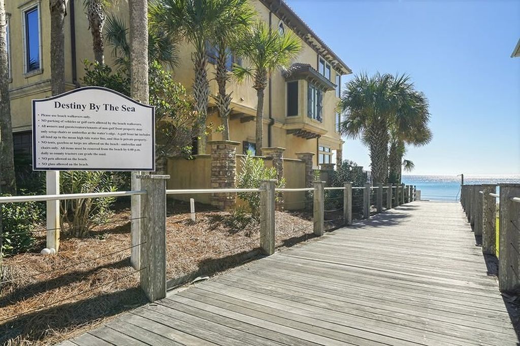 Une promenade en bois mène à un bâtiment sur lequel est apposée une enseigne indiquant « Destiny By The Sea », le tout étant entouré de palmiers et offrant une vue dégagée sur l’océan.
