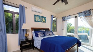 A bedroom with a large bed, a nightstand, a lamp, and a view of the outdoors through a sliding door.