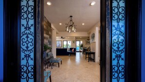 A spacious living room with a sofa, chairs, and a coffee table. There is a chandelier hanging from the ceiling and a door with decorative glass panels.