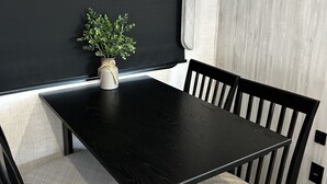 Un coin repas avec une table noire, quatre chaises, une plante en pot et un luminaire noir au plafond.